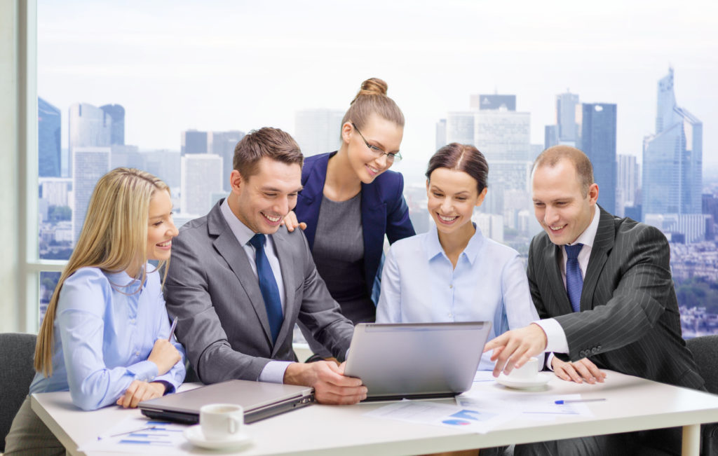 business, technology, teamwork and people concept - smiling business team with laptop computers, documents and coffee having discussion over office background